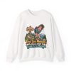 Front of the white unisex sweatshirt printed with a worn-out hiker clutching her knees beside a wooden MODERATE trail sign, with pine trees and snowy mountains and the words "Trail Said Moderate. My Knees Want To Speak To The Manager."