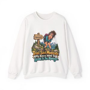 Front of the white unisex sweatshirt printed with a worn-out hiker clutching her knees beside a wooden MODERATE trail sign, with pine trees and snowy mountains and the words "Trail Said Moderate. My Knees Want To Speak To The Manager."