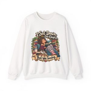 Front of the white unisex sweatshirt printed with a blissful reader curled up with an open book and a sleeping cat between tall stacks of old books and the words "I Sat Down For One Chapter. That Was Tuesday."