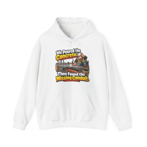 White hoodie printed on the front with a horrified construction worker in a hard hat and hi-vis vest kneeling on a fresh concrete slab, with orange conduit visible buried in the gravel below and the words "We Poured the Concrete. Then Found the Missing Conduit."