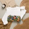 White crewneck sweatshirt with "Still Looking for My Disc" disc golf graphic, lifestyle flat-lay
