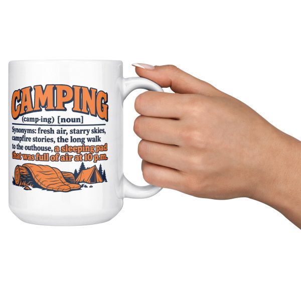 15 oz white ceramic camping mug printed with an orange and navy CAMPING dictionary entry ending "a sleeping pad that was full of air at 10 p.m.", raised in hand