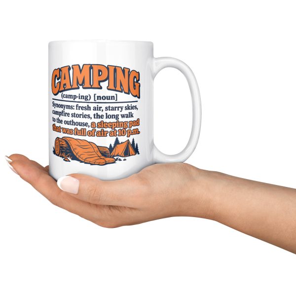 15 oz white ceramic camping mug printed with an orange and navy CAMPING dictionary entry ending "a sleeping pad that was full of air at 10 p.m.", held in an open hand