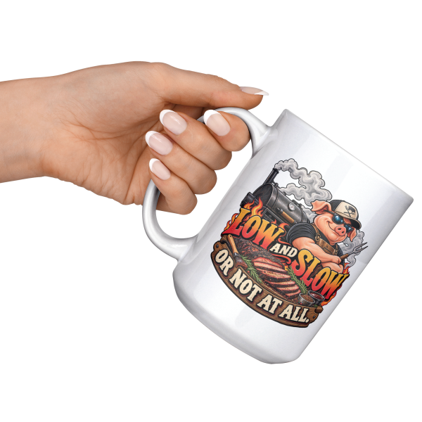 15oz white BBQ mug with a cool pig in sunglasses at a smoking offset smoker, with flame lettering, held at an angle
