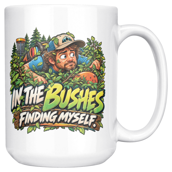 15oz white ceramic disc golf mug printed with IN THE BUSHES FINDING MYSELF and a disc golfer in a cap peering out of dense green bushes with leaves