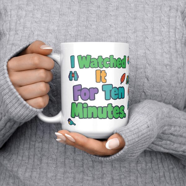 "I watched it for ten minutes. It was a leaf." Birding 15oz mug, held at chest 15 oz white ceramic birding mug, "I watched it for ten minutes" on one side and "It was a leaf" on the other, with birds, binoculars and leaves, held at chest