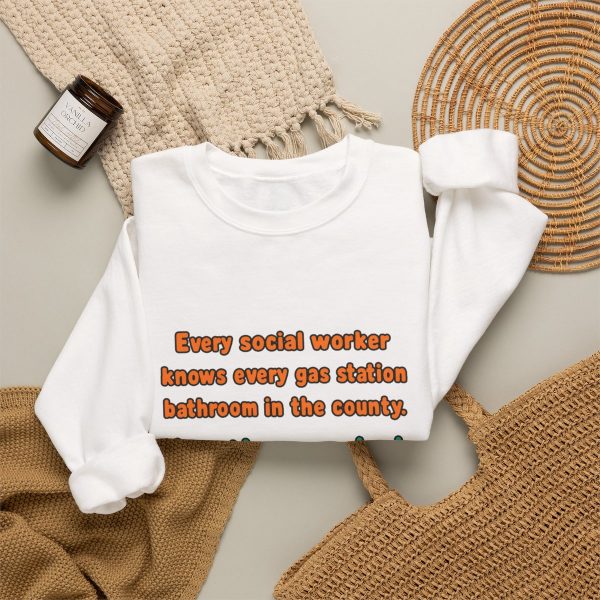 White flat vector crewneck sweatshirt with the social work dictionary joke: Knows every gas station bathroom in the county. Has them ranked., folded view