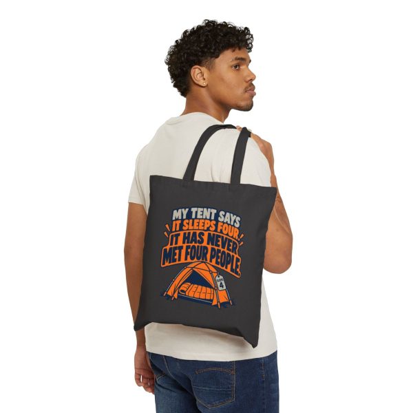 Model carrying the tote on one shoulder, front print showing. Black flat vector tote bag with the camping tent joke: My tent says it sleeps four. It has never met four people.