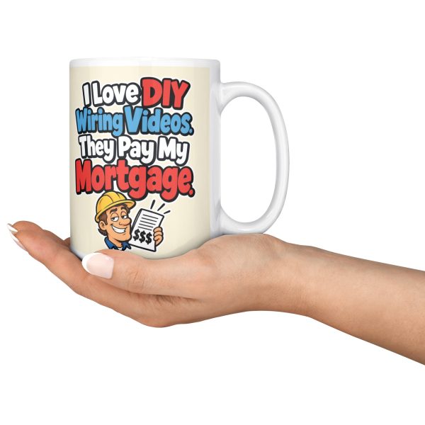 15 oz white ceramic electrician mug printed with "I Love DIY Wiring Videos. They Pay My Mortgage.", held in an open hand